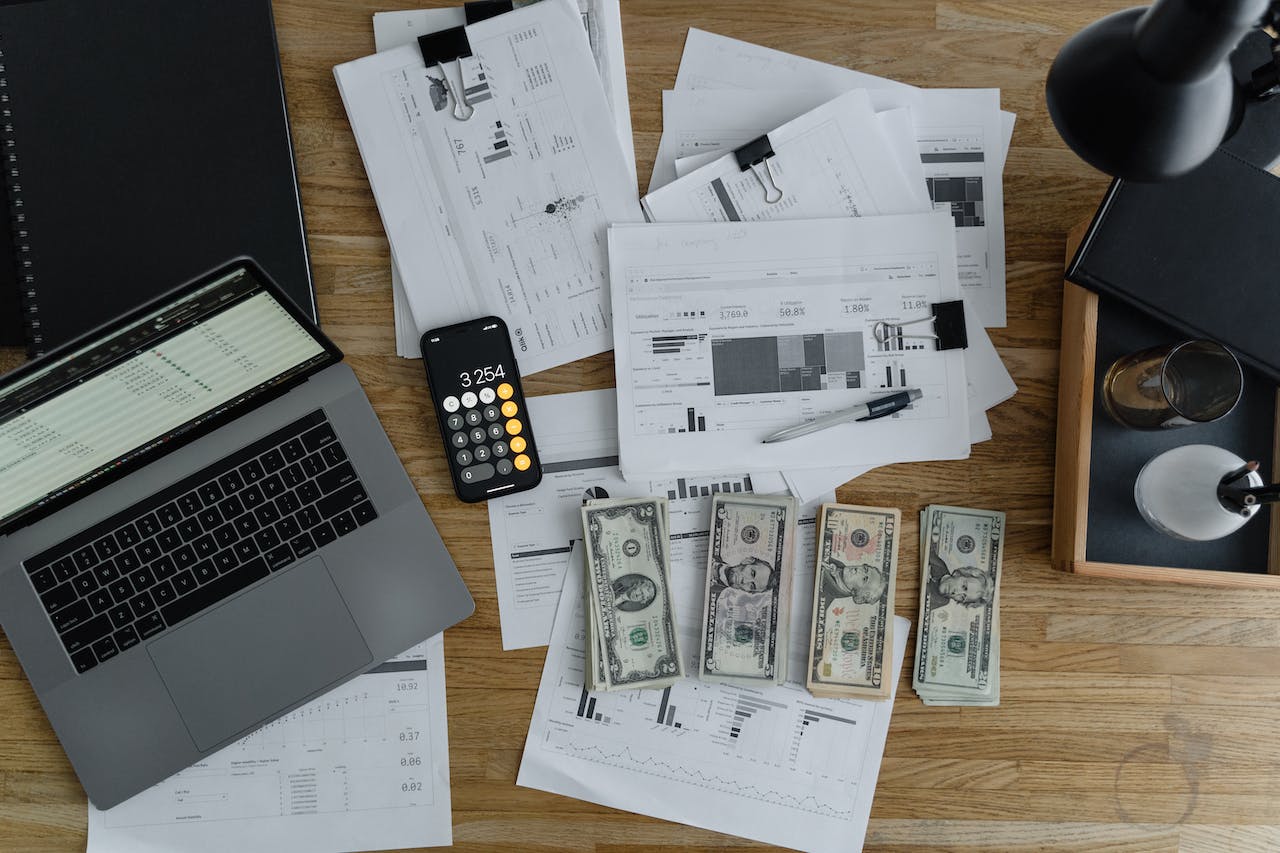 https://www.pexels.com/photo/a-laptop-near-the-dollars-and-papers-on-a-wooden-table-6693655/